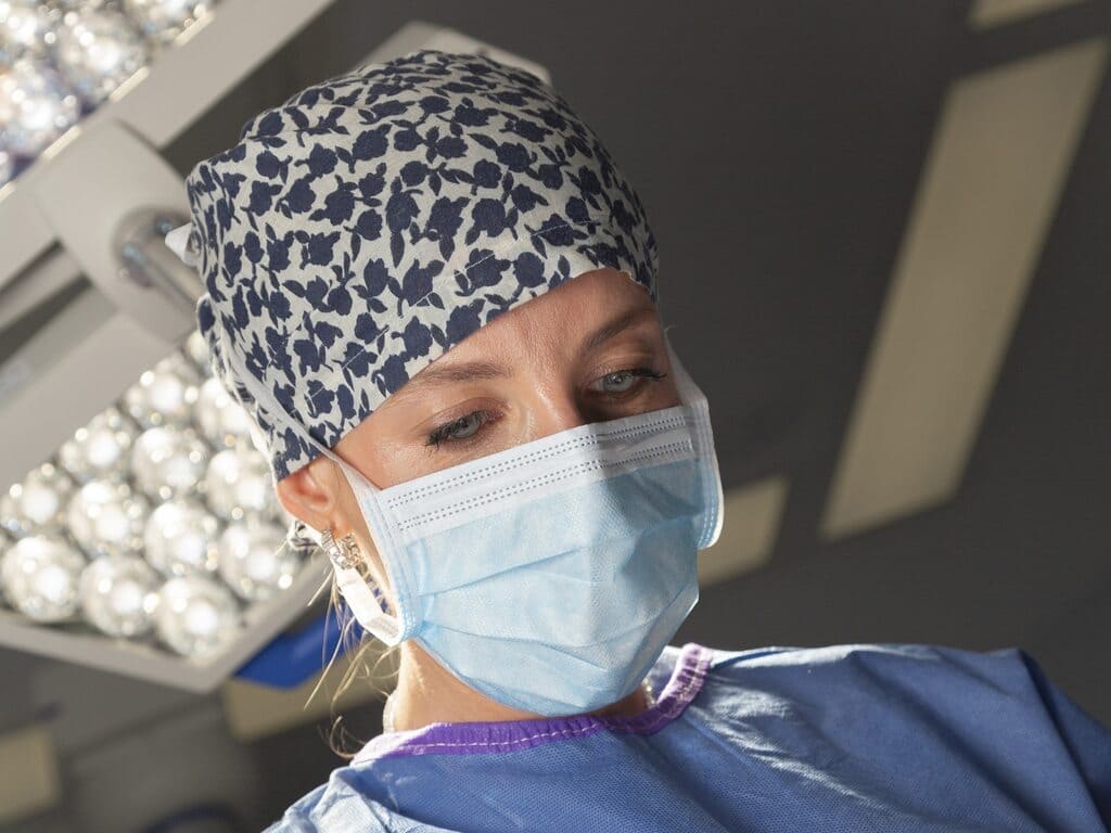 Doctora cirujana con mascarilla y gorro de operación azul.