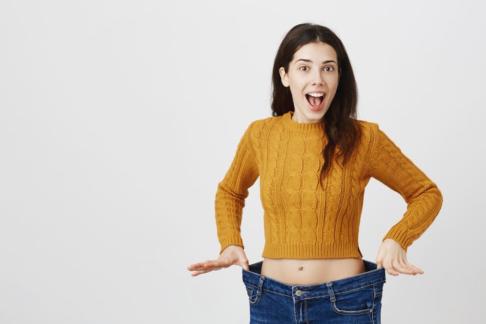 mujer sorprendida mostrando cintura delgada con sueter color mostaza sobre fondo blanco